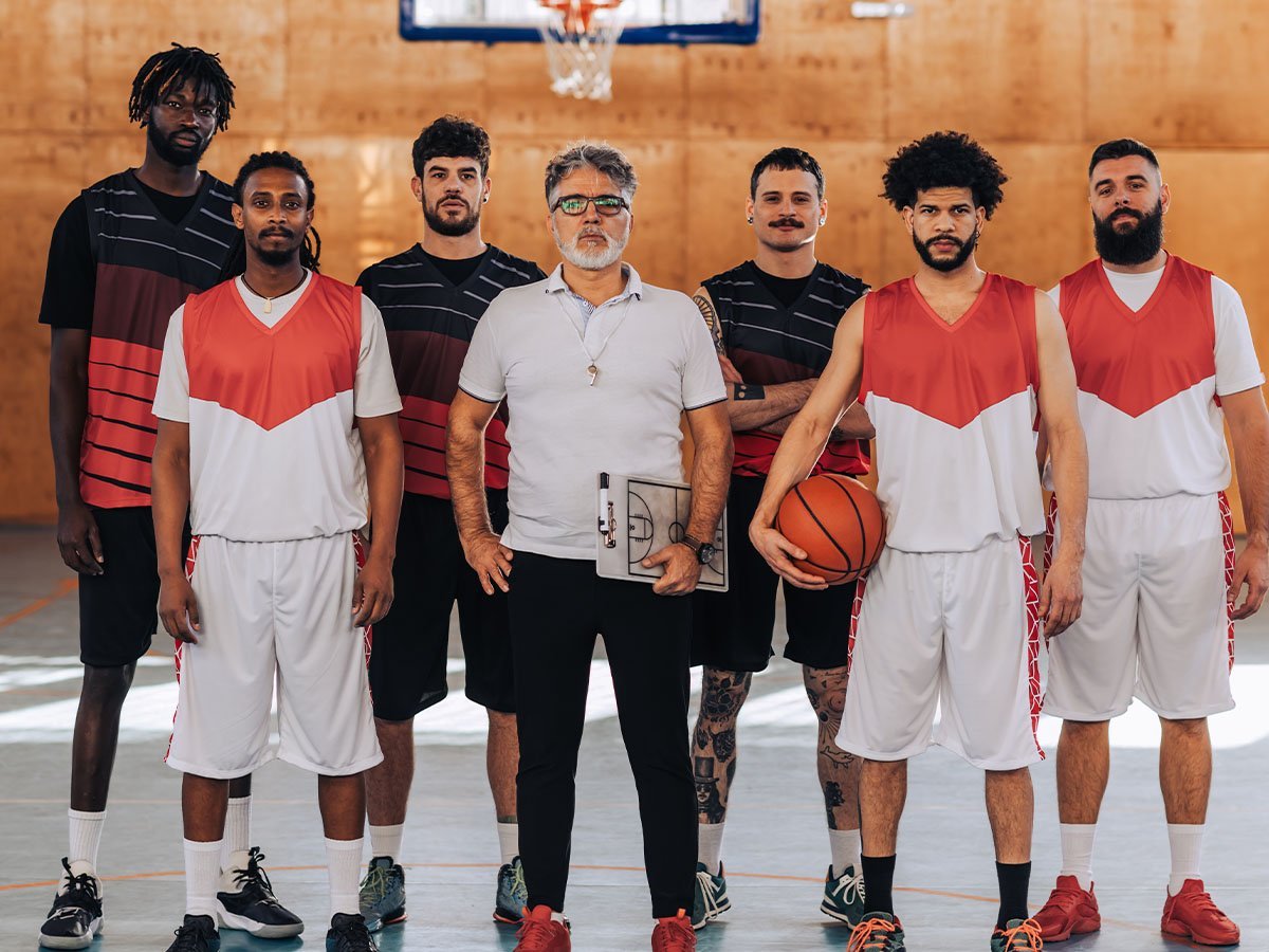 Equipo de básquet con camisetas y shorts del club, junto a su entrenador, en el gimnasio