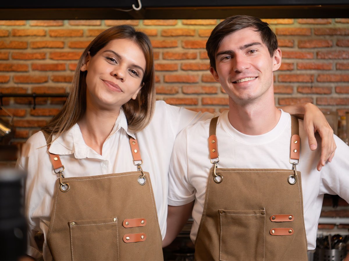 Dos empleados de un local con delantal de trabajo y remera blanca